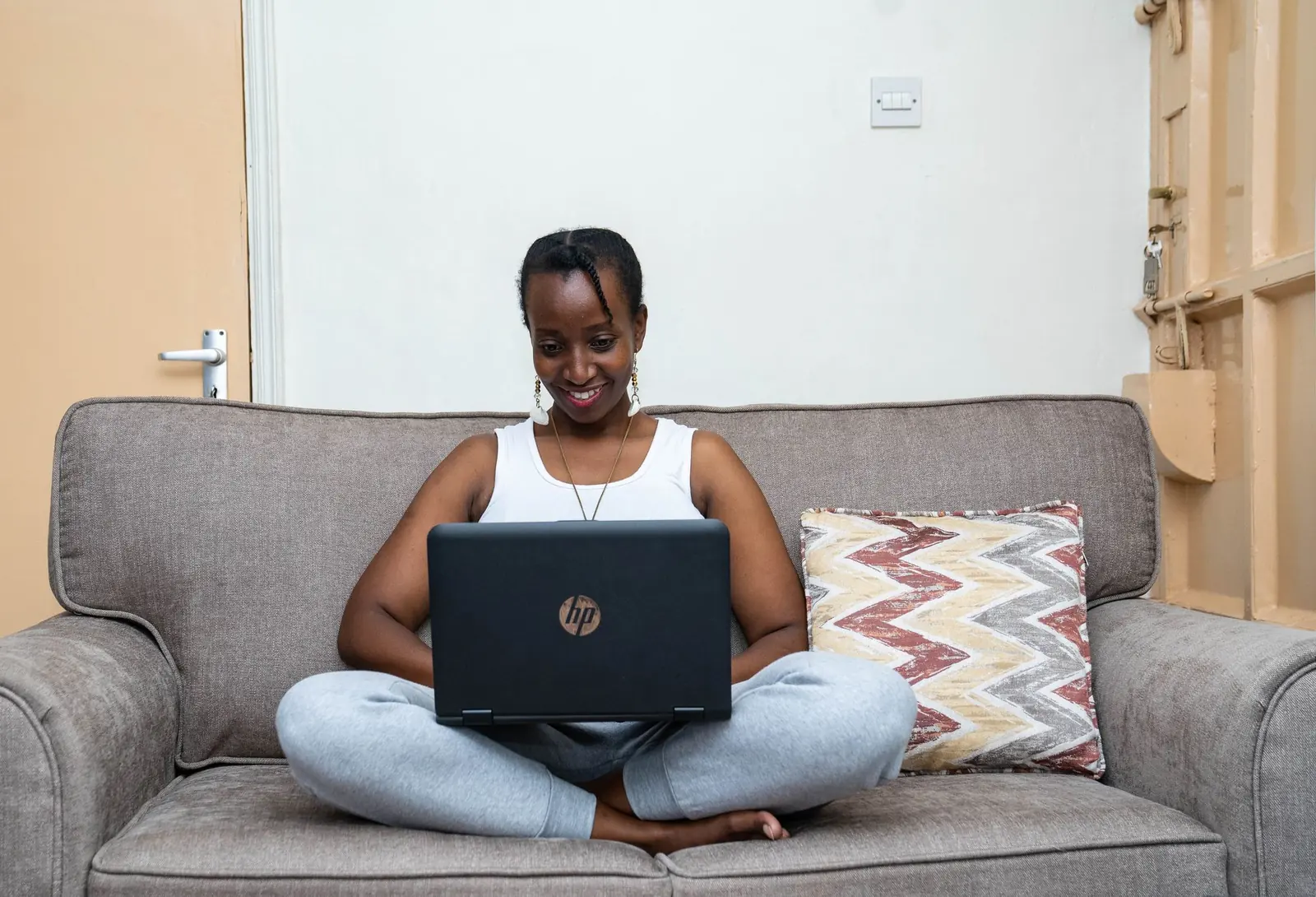 A woman smiling at her laptop on a sofa at home